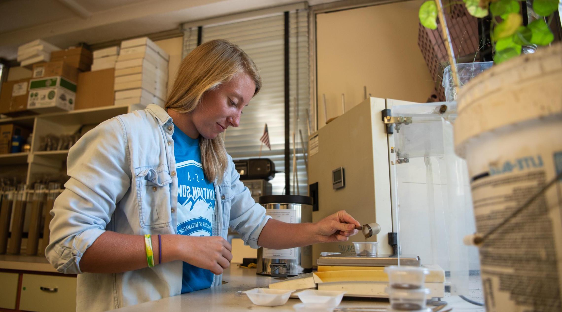 实验室里的一位年轻女子将少量土壤倒进一个透明的塑料杯中.